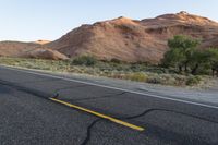 a empty roadway between some cliffs near by trees and bushes, with a yellow line