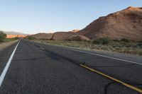 a empty roadway between some cliffs near by trees and bushes, with a yellow line