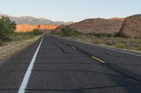 a empty roadway between some cliffs near by trees and bushes, with a yellow line