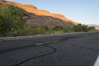 a empty roadway between some cliffs near by trees and bushes, with a yellow line