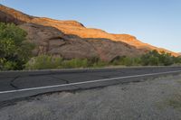 a empty roadway between some cliffs near by trees and bushes, with a yellow line