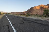 a empty roadway between some cliffs near by trees and bushes, with a yellow line