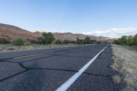 an empty roadway in the middle of nowhere, with no traffic to travel, and some vegetation, mountains, grass, and shrubs