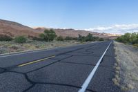 an empty roadway in the middle of nowhere, with no traffic to travel, and some vegetation, mountains, grass, and shrubs