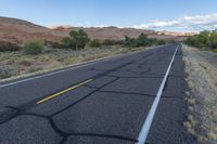 an empty roadway in the middle of nowhere, with no traffic to travel, and some vegetation, mountains, grass, and shrubs