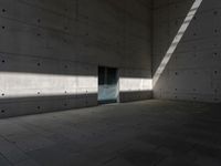 a empty room with a concrete wall and a red fire hydrant in it, as the sun shines on the stone floor
