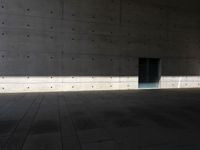 a empty room with a concrete wall and a red fire hydrant in it, as the sun shines on the stone floor