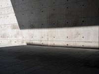 a empty room with a concrete wall and a red fire hydrant in it, as the sun shines on the stone floor