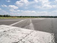 an empty runway is seen from the ground in daylight light with clouds in the sky