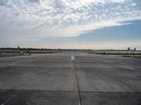 an empty runway with a single airplane sitting out in the distance under a partly cloudy sky