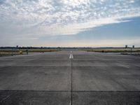 an empty runway with a single airplane sitting out in the distance under a partly cloudy sky