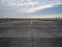 an empty runway with a single airplane sitting out in the distance under a partly cloudy sky