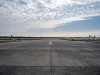 an empty runway with a single airplane sitting out in the distance under a partly cloudy sky