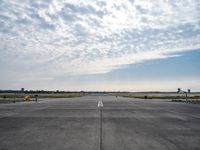 an empty runway with a single airplane sitting out in the distance under a partly cloudy sky