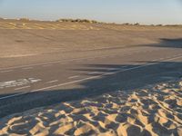 a large empty runway that is going towards the desert and the field to the side