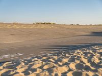 a large empty runway that is going towards the desert and the field to the side