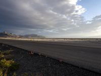 an empty runway with dramatic skies and mountains in the back ground of an airport on a cloudy day