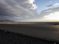 an empty runway with dramatic skies and mountains in the back ground of an airport on a cloudy day