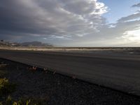 an empty runway with dramatic skies and mountains in the back ground of an airport on a cloudy day