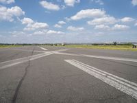 an empty runway in the daytime with fluffy white clouds overhead the road is full of planes