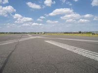 an empty runway in the daytime with fluffy white clouds overhead the road is full of planes