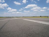 an empty runway in the daytime with fluffy white clouds overhead the road is full of planes