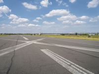 an empty runway in the daytime with fluffy white clouds overhead the road is full of planes