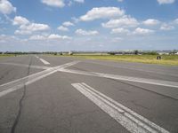 an empty runway in the daytime with fluffy white clouds overhead the road is full of planes