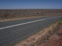 an empty highway with double lines marking the sides of the road in the distance are scrubby grass and sparse shrubs