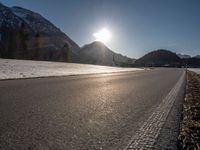 an empty rural road is shown in front of the mountains during wintertime with the sun peeking over the top