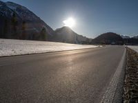 an empty rural road is shown in front of the mountains during wintertime with the sun peeking over the top