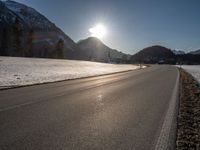 an empty rural road is shown in front of the mountains during wintertime with the sun peeking over the top