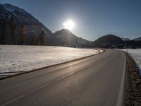 an empty rural road is shown in front of the mountains during wintertime with the sun peeking over the top