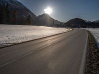 an empty rural road is shown in front of the mountains during wintertime with the sun peeking over the top