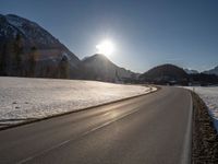 an empty rural road is shown in front of the mountains during wintertime with the sun peeking over the top