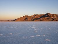 an empty salt plain surrounded by snow covered mountains in the sunset time of day and pink light