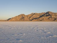 an empty salt plain surrounded by snow covered mountains in the sunset time of day and pink light