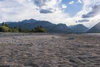 an empty sandy beach in a mountainous area under a blue sky with clouds and a mountain range