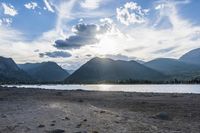 an empty sandy beach in a mountainous area under a blue sky with clouds and a mountain range