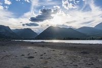 an empty sandy beach in a mountainous area under a blue sky with clouds and a mountain range