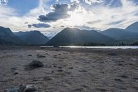 an empty sandy beach in a mountainous area under a blue sky with clouds and a mountain range