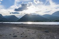 an empty sandy beach in a mountainous area under a blue sky with clouds and a mountain range