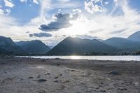an empty sandy beach in a mountainous area under a blue sky with clouds and a mountain range