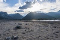 an empty sandy beach in a mountainous area under a blue sky with clouds and a mountain range