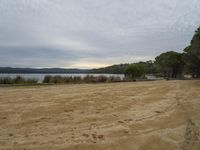 the sandy beach is empty in the middle of the day overlooking a lake and a distant forest