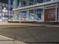 an empty sidewalk in front of a glassed building with two lights in the corner