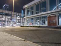 an empty sidewalk in front of a glassed building with two lights in the corner