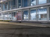 an empty sidewalk in front of a glassed building with two lights in the corner