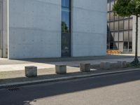 an empty sidewalk next to a tall building on a city street with no cars and a man sitting in a chair