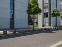 an empty sidewalk next to a tall building on a city street with no cars and a man sitting in a chair